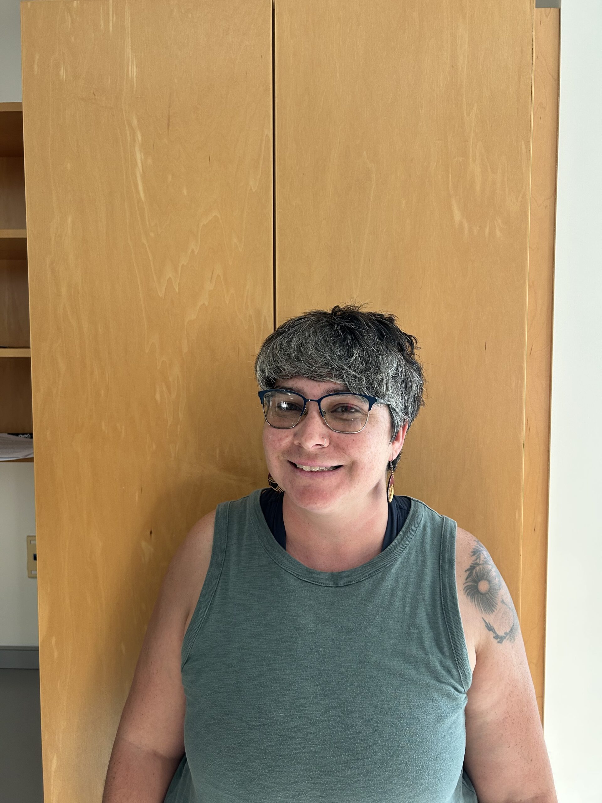 Nina has short grayish hair, wears glasses, and is smiling in a green dress.